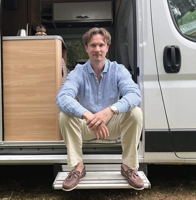 Alex sitzt im Türrahmen seines weißen Campervans